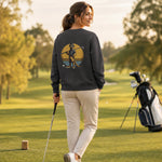 Eine hübsche junge Frau auf dem Golfplatz trägt ein graues Sweatshirt von Sporty Animals mit einem lustigen Erdmännchen-Motiv auf dem Rücken, das einen Golfschläger hält