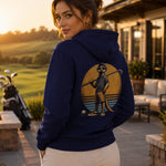 Eine junge hübsche frau steht auf der Terrasse und blickt auf den Golfplatz. Sie trägt einen stylischen Hoodie von Sporty Animals mit einem Erdmännchen, das lässig einen Golfschläger auf seiner Schulter hält.